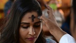 Ein Priester zeichnet einer Katholikin ein Aschekreuz auf die Stirn