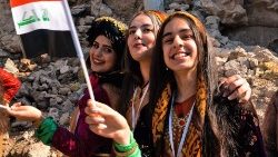 (file photo) Young women dressed in traditional clothing wave an Iraqi national flag during Pope Francis 2021 visit to Iraq