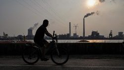 FILE PHOTO: A man riding a bicycle across a coal power plant in Shanghai. Coal consumption releases deadly levels of air pollution. 