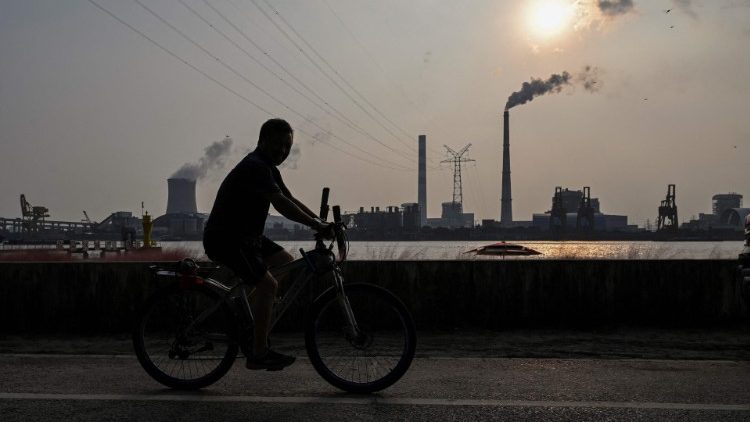 FILE PHOTO: A man riding a bicycle across a coal power plant in Shanghai. Coal consumption releases deadly levels of air pollution. 