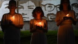 सन सल्वाडोर में येसु समाजी शहीदों की तस्वीर के सामने जलती मोमबत्ती लिये उत्सव में भाग लेते लोग