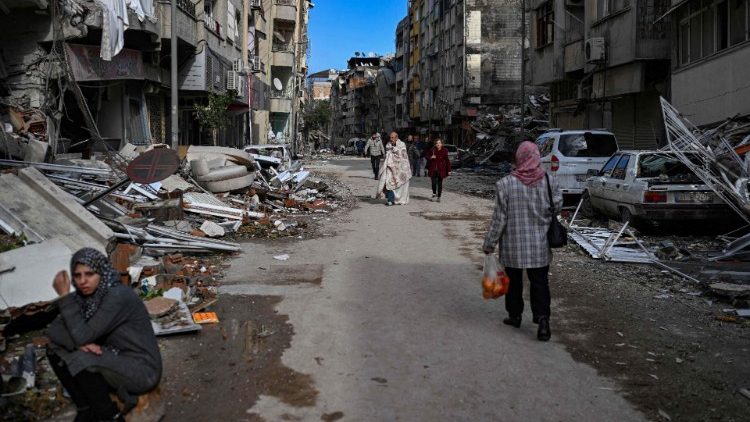People walk along a street strewn with debris as they look for relatives in the Hatay 