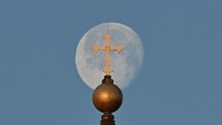 Cruz no topo da Basílica de São Pedro tendo ao funfo a lua. (Photo by AFP/Alberto Pizzoli)