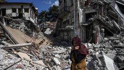 तुर्की में भुकम्प के कारण ध्वस्त मलबे के सामने खड़ी एक महिला