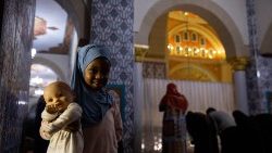 Pětileté děvčátko pózuje pro fotografii s panenkou v ruce, zatímco se muslimští věřící modlí během prvního dne měsíce ramadánu v mešitě Nizamiye v jihoafrickém Midrandu