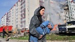 mulher passa por prédios residenciais danificados enquanto carrega uma criança em Uman, cerca de 215 km ao sul de Kiev, em 28 de abril de 2023. (Foto de Sergei SUPINSKY / AFP)