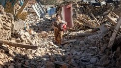 A woman walks past destroyed houses in the village of Tafeghaghte