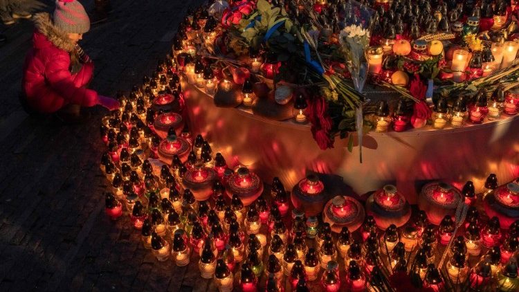 Uma criança coloca uma vela na estátua infantil 'Memória Amarga da Infância', enquanto as pessoas prestam homenagem às vítimas da fome de 1932-1933 no Museu Nacional do Holodomor-Genocídio em Kiev. (Photo by Roman PILIPEY / AFP)