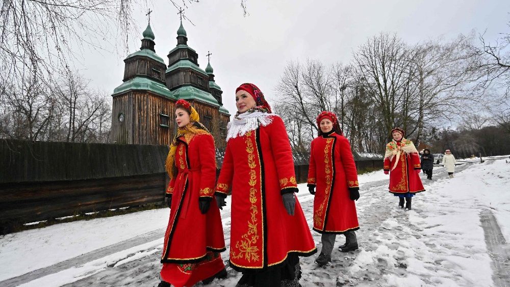 Mulheres, vestindo roupas tradicionais ucranianas, caminham por uma rua coberta de neve enquanto participam das celebrações de Natal na vila de Pyrogove, perto de Kiev, em 25 de dezembro de 2023, em meio à invasão russa na Ucrânia. A Ucrânia celebra o Natal em 25 de dezembro de 2023 pela primeira vez, depois de o governo ter alterado a data de 7 de janeiro, data em que a maioria dos crentes ortodoxos celebra, numa afronta à Rússia. (Foto de Sergei SUPINSKY/AFP)