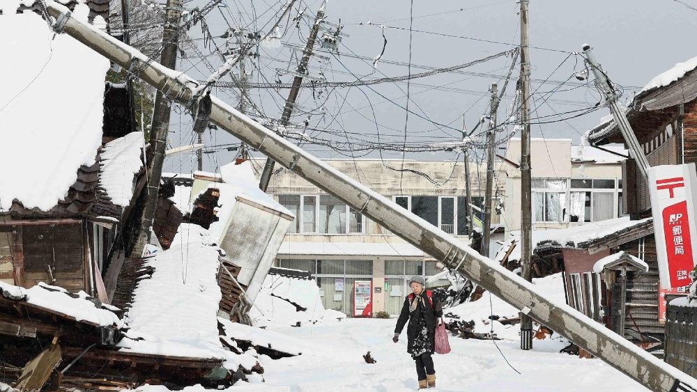 Japonesa caminha em estrada nevada em meio à destruição na cidade de Suzu, província de Ishikawa. (Photo by JIJI Press / AFP) 