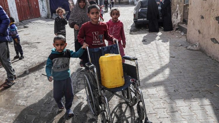 रफाह में बच्चे ह्वील चेयर में पानी  से भरा ड्रम ले जाते हुए