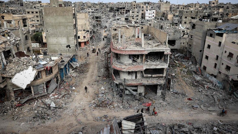 Palestinos passam por prédios destruídos em Khan Yunis, depois que Israel retirou suas forças terrestres do sul da Faixa de Gaza (AFP)