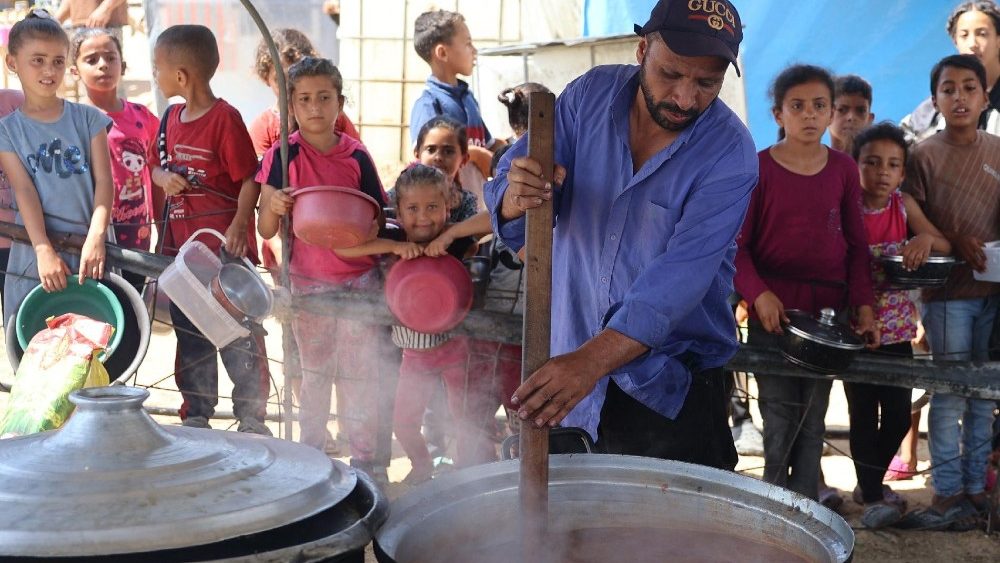 Crianças aguardam a distribuição de alimentos em um acampamento, onde vivem devido ao bombardeio israelense na Faixa de Gaza (AFP)