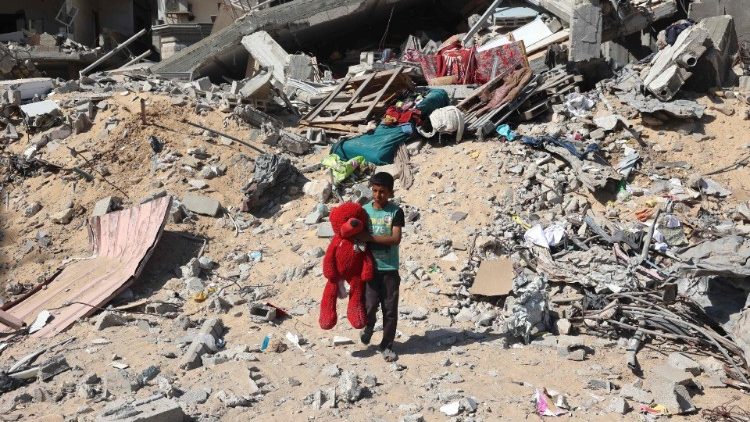 Un niño palestino camina con un oso de peluche recuperado de entre los escombros de un edificio destruido tras un bombardeo