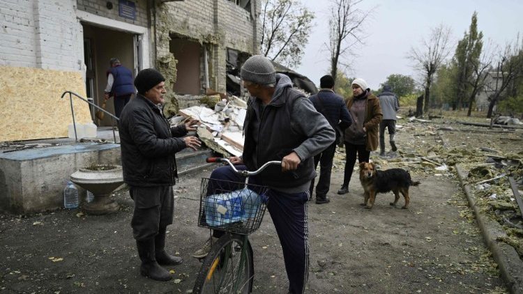 Moradores locais conversam em frente a um prédio administrativo local, destruído após um ataque no vilarejo de Shevchenkove, perto da cidade de Pokrovsk, região de Donetsk, em 20 de outubro de 2024, em meio à invasão russa da Ucrânia. (Foto de Genya SAVILOV / AFP)