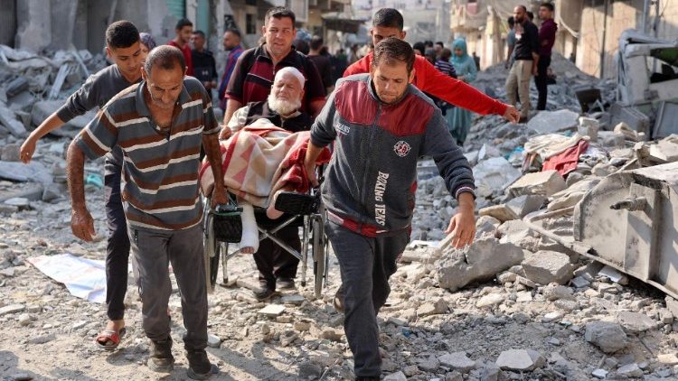 Uomini palestinesi trasportano un anziano in sedia a rotelle tra le macerie del campo profughi di Jabalya, nel nord della Striscia di Gaza (Afp)