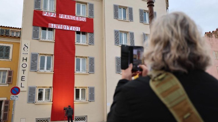 A woman takes a picture of a red cross hung outside a hotel in Ajaccio