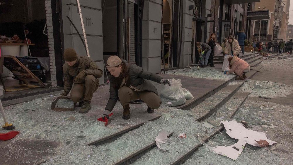 Pessoas limpam cacos de vidro no local de um ataque de míssil em Kiev em 20 de dezembro de 2024, em meio à invasão russa da Ucrânia. Mísseis russos miraram a capital ucraniana Kiev ao nascer do sol em 20 de dezembro de 2024, matando pelo menos uma pessoa e cortando o aquecimento de centenas de prédios residenciais em baixas temperaturas. (Foto de Roman PILIPEY / AFP)