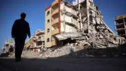 गज़ा में ध्वस्त इमारत के पास खड़ा एक व्यक्ति