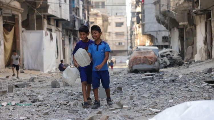 Crianças palestinas segurando recipientes de água caminham sobre os escombros de um prédio alvo de um ataque israelense no bairro de Sheikh Radwan, na Cidade de Gaza, no centro da Faixa de Gaza, em 6 de julho de 2025.. (Foto de Eyad BABA / AFP)