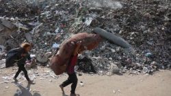 Palestinian children carry their belongings past an unexploded missile in a rubbish dump in Gaza City