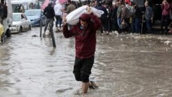 गज़ा में एक बाढ़ के बीच कंधे पर समान ले जाते हुए