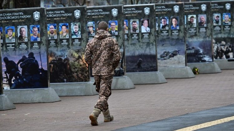 Militar ucraniano caminha ao lado de retratos no Beco dos Her&oacute;is Ca&iacute;dos, em um distrito de Kiev, em 7 de dezembro de 2025, em meio &agrave; invas&atilde;o russa na Ucr&acirc;nia. (Foto de Sergei SUPINSKY / AFP)