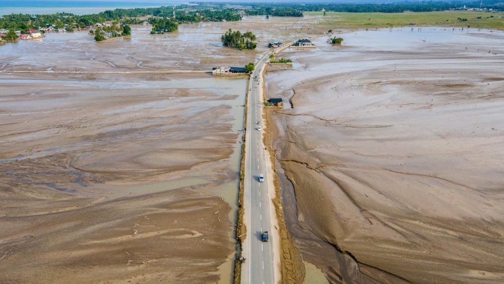 Uma vista aérea mostra passageiros passando por campos de arroz inundados de lama após enchentes repentinas em Meureudu, no distrito de Pidie Jaya, província de Aceh, Indonésia, em 8 de dezembro de 2025. Regiões atingidas por enchentes que mataram centenas de pessoas na Indonésia sofriam com a escassez de alimentos e medicamentos, disseram as autoridades, enquanto elefantes ajudavam na limpeza dos destroços em 8 de dezembro. (Foto de Chaideer MAHYUDDIN / AFP)