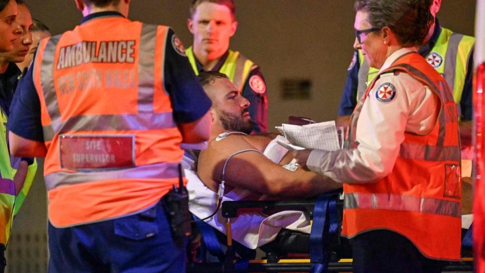Profissionais de saúde transportam um homem em uma maca para uma ambulância após um tiroteio na praia de Bondi, em Sydney, em 14 de dezembro de 2025. A polícia australiana informou que duas pessoas foram detidas após relatos de múltiplos disparos em 14 de dezembro na famosa praia de Bondi, em Sydney, e pediu à população que se abrigasse. (Foto de Saeed Khan / AFP)