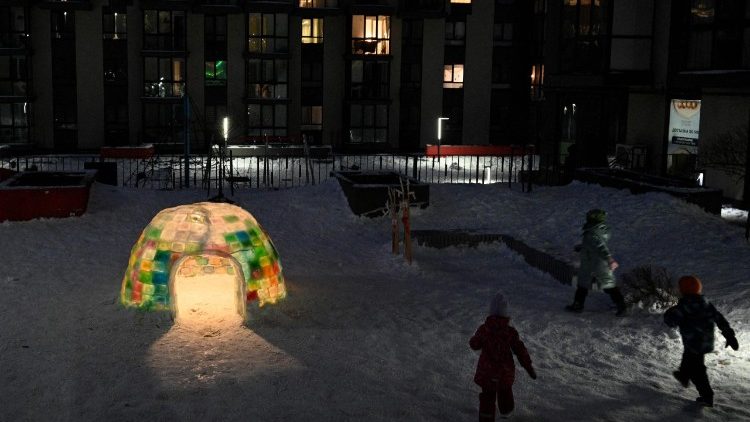 Crian&ccedil;as brincam ao lado de um iglu de gelo constru&iacute;do por moradores locais no p&aacute;tio de um pr&eacute;dio residencial em Lviv, em 18 de janeiro de 2026, em meio &agrave; invas&atilde;o russa da Ucr&acirc;nia. (Foto de YURIY DYACHYSHYN / AFP)