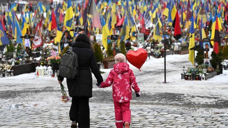 Uma m&atilde;e e sua filha caminham segurando um bal&atilde;o em forma de cora&ccedil;&atilde;o no Cemit&eacute;rio Militar de Lychakiv, em Lviv, no Dia dos Namorados, em 14 de fevereiro de 2026, em meio &agrave; invas&atilde;o russa da Ucr&acirc;nia. (Foto de YURIY DYACHYSHYN / AFP)
