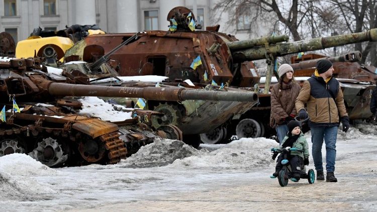 Um casal e um menino passeiam de bicicleta pela exposi&ccedil;&atilde;o a c&eacute;u aberto de equipamentos militares russos destru&iacute;dos em Kiev, em 15 de fevereiro de 2026, em meio &agrave; invas&atilde;o russa na Ucr&acirc;nia. (Foto de Sergei SUPINSKY / AFP)