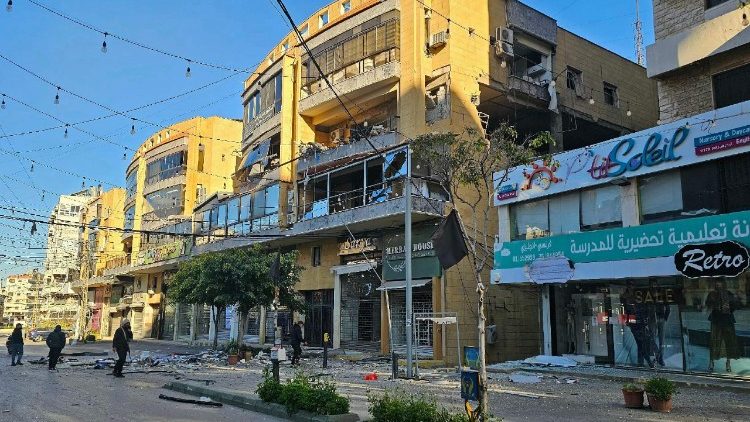 Pessoas passam por edif&iacute;cios danificados ap&oacute;s ataques a&eacute;reos no bairro de Ghobeiry, no sub&uacute;rbio sul de Beirute, nesta quinta (05/03)