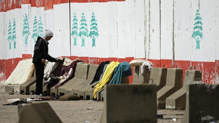 A displaced man puts his laundry on the sidewalk's concrete blocks at a parking lot in Beirut's waterfront area