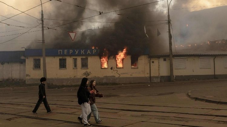Pessoas caminham ao lado de pr&eacute;dios danificados e em chamas ap&oacute;s ataques russos em Kiev, em 24 de maio de 2026, em meio &agrave; invas&atilde;o russa da Ucr&acirc;nia. Um grande ataque com m&iacute;sseis bal&iacute;sticos atingiu Kiev na madrugada de 24 de maio, disseram as autoridades, ferindo pelo menos cinco pessoas, depois que Moscou amea&ccedil;ou retaliar pelos ataques no leste da Ucr&acirc;nia, ocupado pela R&uacute;ssia. (Foto de Roman PILIPEY / AFP)