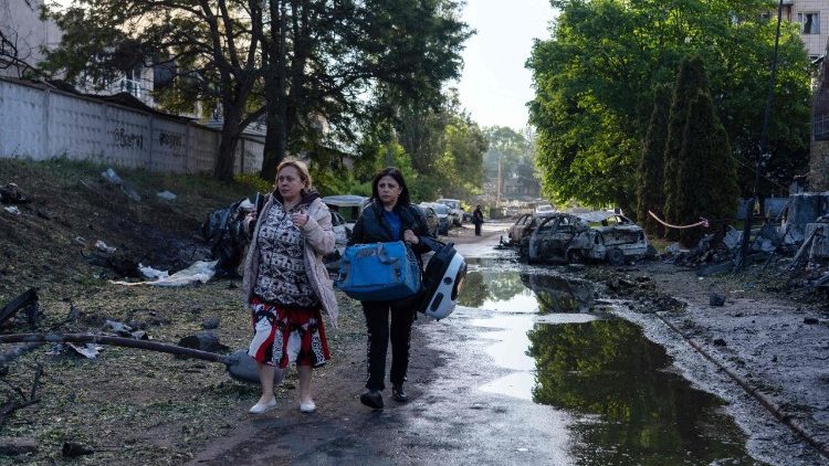 Moradores locais carregam alguns pertences enquanto caminham por entre carros destru&iacute;dos e escombros no local de um ataque a&eacute;reo em Kiev, em 2 de junho de 2026, em meio &agrave; invas&atilde;o russa da Ucr&acirc;nia. (Foto de OLEKSII FILIPPOV / AFP)