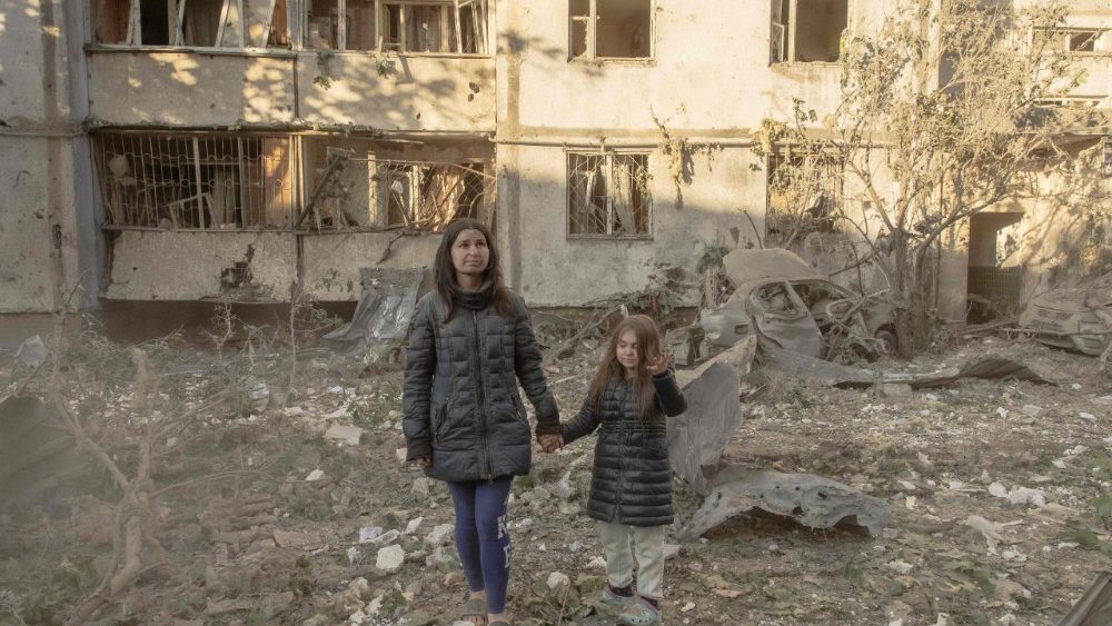 Olha Mudra caminha com sua filha de 6 anos, Nataliia, perto do prédio residencial onde moram, que foi danificado durante os ataques maciços de mísseis e drones russos contra Kiev em 2 de junho de 2026, em meio à invasão russa da Ucrânia. Bombardeios de mísseis e drones russos atingiram partes da Ucrânia, matando quatro pessoas e ferindo dezenas, disseram autoridades, nos ataques mais recentes de uma guerra que não dá sinais de terminar. (Foto de Roman PILIPEY / AFP) 