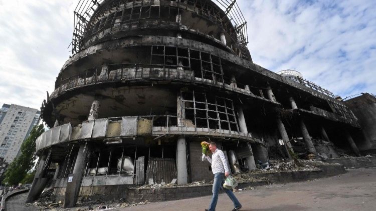 Um homem carrega flores enquanto caminha em frente a um shopping center em Kiev destru&iacute;do durante um ataque russo com drones e m&iacute;sseis, em 18 de junho de 2026, em meio &agrave; invas&atilde;o russa na Ucr&acirc;nia. (Foto de Sergei SUPINSKY / AFP)