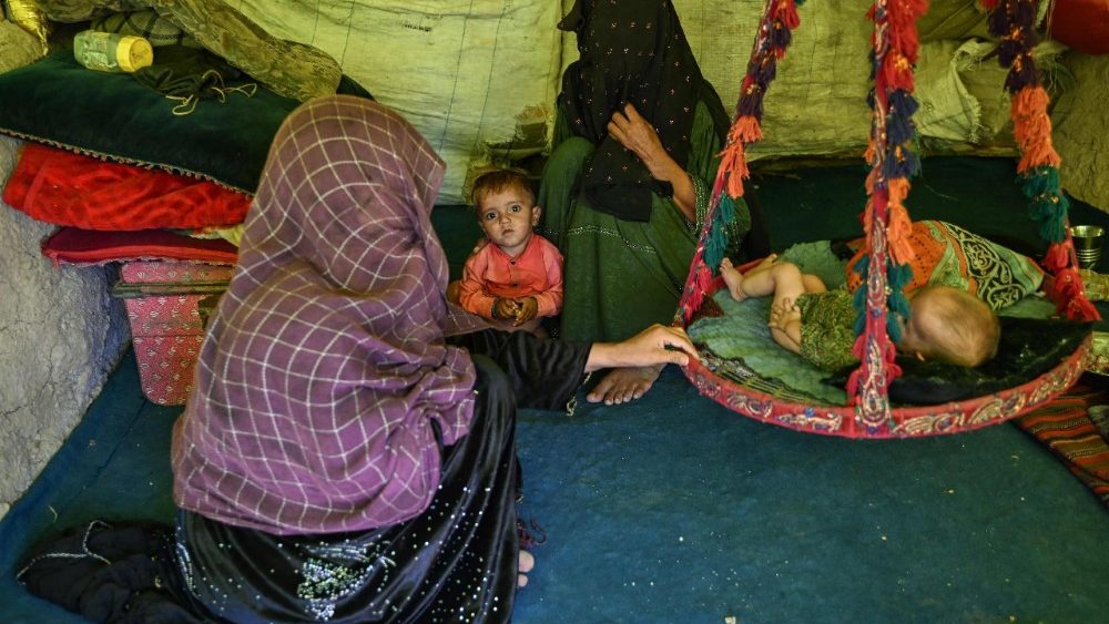 Mulheres refugiadas afegãs, juntamente com crianças, sentam-se dentro de um abrigo improvisado em um campo de refugiados em Nasaji Pul, em Kandahar, em 20 de junho de 2026. (Foto de Sanaullah SEIAM / AFP)