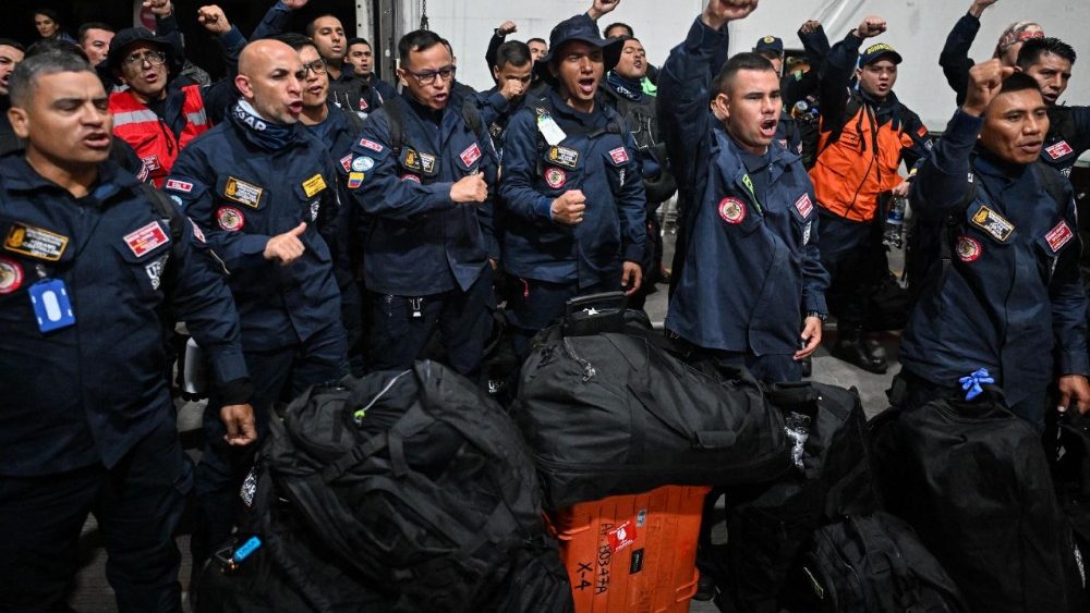 Membros da equipe colombiana de Busca e Resgate Urbano (USAR) gritam slogans antes de partirem com ajuda humanitária para a Venezuela na Base Aérea de Catam, em Bogotá, em 26 de junho de 2026, após terremotos devastadores. Venezuelanos desesperados correram para encontrar e resgatar entes queridos presos sob os escombros de prédios desabados após dois grandes terremotos, de magnitude 7,2 e 7,5, atingirem o norte da Venezuela, matando pelo menos 235 pessoas e deixando mais de 1.500 feridas. (Foto de Luis Acosta / AFP)
