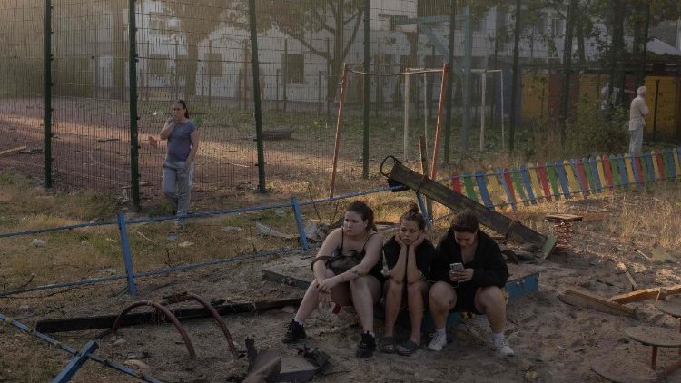 Meninas sentadas em um parquinho infantil enquanto olham para um pr&eacute;dio residencial danificado ap&oacute;s um ataque a&eacute;reo russo &agrave; capital ucraniana, Kiev, em 2 de julho de 2026, em meio &agrave; invas&atilde;o russa na Ucr&acirc;nia. Ataques russos com m&iacute;sseis e drones abalaram Kiev no in&iacute;cio de 2 de julho, matando pelo menos oito pessoas e ferindo dezenas, depois do presidente Volodymyr Zelensky ter avisado que Moscovo estava a preparar um “ataque massivo”. (Foto de Roman PILIPEY/AFP)