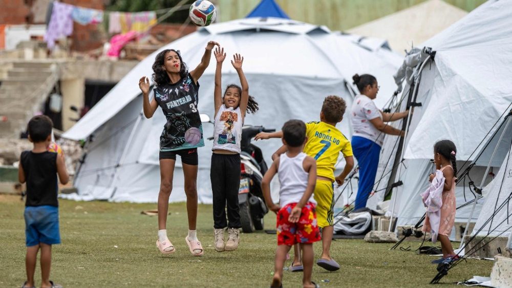 Crianças brincam com uma bola perto de tendas no estádio de beisebol César Nieves, no bairro de La Angustia, em Catia La Mar, estado de La Guaira, Venezuela, em 3 de julho de 2026, onde pessoas deslocadas buscaram refúgio. O número de mortos pelos devastadores terremotos gêmeos na Venezuela subiu para 2.645, com mais de 12.600 feridos, segundo novos dados oficiais divulgados em 3 de julho. (Foto de Miguel MEDINA / AFP)