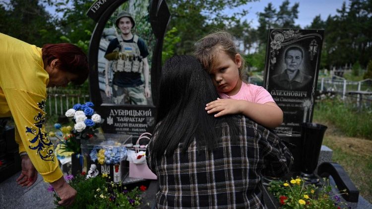 Nadia (E), 57, m&atilde;e do falecido militar ucraniano Andriy Dubnytsky, sua vi&uacute;va Liudmyla (C), 27, e sua filha Mia (D), 4, visitam seu t&uacute;mulo em um cemit&eacute;rio na vila de Stepantsi, regi&atilde;o de Cherkasy, em 7 de julho de 2026, em meio &agrave; invas&atilde;o russa da Ucr&acirc;nia. Na &uacute;ltima mensagem que Liudmyla Dubnytska recebeu do marido, ele disse que provavelmente seria capturado pelas for&ccedil;as russas. Dois dias depois, ela reconheceu o corpo dele em um v&iacute;deo nas redes sociais de um grupo de soldados ucranianos mortos. (Foto de Genya SAVILOV / AFP)