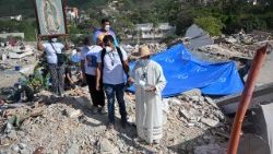 Um padre asperge água benta sobre os escombros de um prédio desabado enquanto uma mulher segura uma imagem da Virgem de Guadalupe e outros fiéis observam de perto em Caraballeda, Venezuela, em 17 de julho de 2026, após os terremotos de 24 de junho. (Foto de Juan Barreto / AFP)