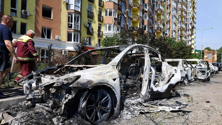 Personas caminan junto a vehículos dañados estacionados en una calle tras los ataques con misiles en Kyiv, el 19 de julio de 2026, en el contexto de la invasión rusa de Ucrania.
