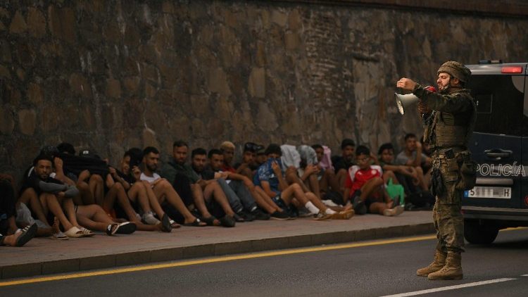Un soldato spagnolo parla ai migranti seduti sul marciapiede prima di scortarli nel ritorno in Marocco, dall'enclave di Ceuta