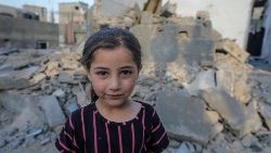 गाजा पट्टी में फिलिस्तीनी बच्ची अपने टूटे पड़े घर के सामने खड़ी है