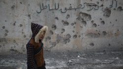 Ein Kind läuft an einer beschädigten Wand mit der Aufschrift "Wenn du nicht die Wahrheit sagen kannst, applaudiere nicht für die Lüge" vorbei, nachdem Granaten auf ein Wohngebiet in der Stadt Daret Azzah im Umland von Aleppo, Syrien, gefallen sind, 1. Januar 2024. 