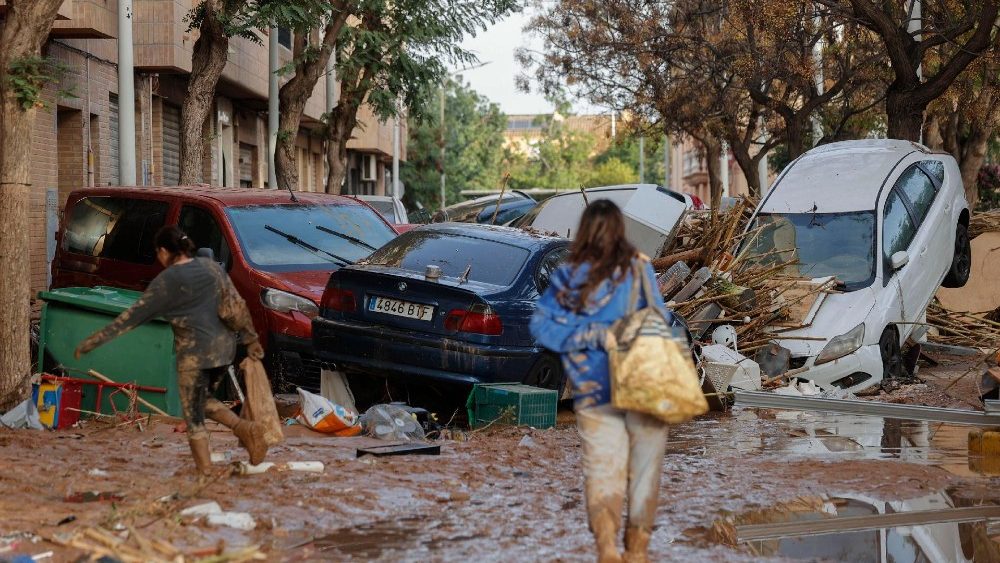 Moradores caminham por uma rua coberta de lama ao lado de carros empilhados no município de Paiporta, atingido por enchentes, na província de Valência, Espanha, em 30 de outubro de 2024.). EPA/MANUEL BRUQUE