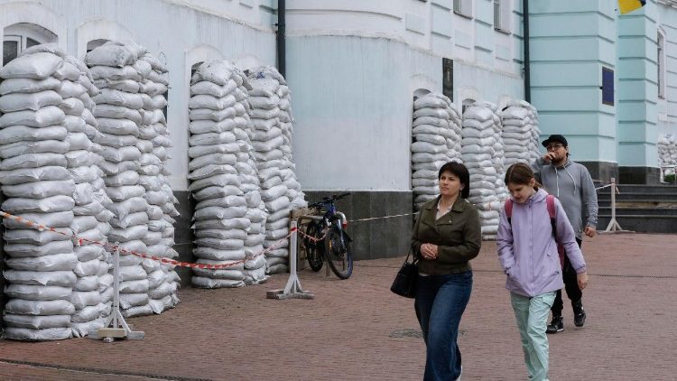 Pessoas passam por um prédio com janelas cobertas por sacos de areia como proteção contra bombardeios no centro de Kiev, Ucrânia, em 20 de maio de 2025. EPA/SERGEY DOLZHENKO